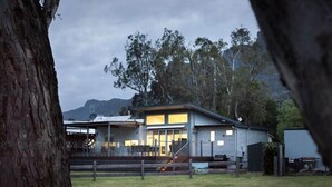 A modern two-story building with large windows and a flat roof, surrounded by trees and a mountain in the background. - Hemley House - Three Bedroom, 2 bathroom House Halls gap (Halls Gap)