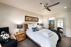 A bedroom with a bed, a nightstand, a chair, a ceiling fan, a mirror, and artwork on the wall.