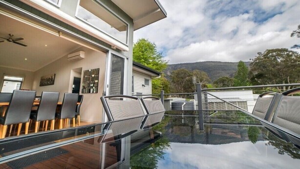 A modern dining area with a glass table and chairs, a ceiling fan, and a view of the surrounding landscape. - Hemley House - Three Bedroom, 2 bathroom House Halls gap (Halls Gap)