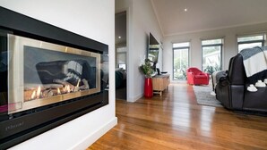 A modern living room with a fireplace, wooden flooring, and a red chair. - Hemley House - Three Bedroom, 2 bathroom House Halls gap (Halls Gap)