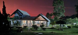 A modern house with a large glass facade, a sloped roof, and a well-maintained garden with pathways and outdoor furniture. - WONDERFUL NATURAL LANDSCAPING (Bofete)