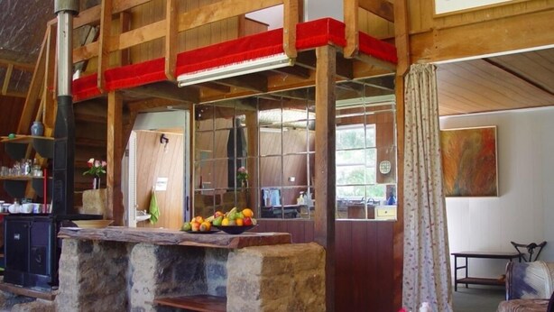 Un intérieur rustique avec un comptoir en pierre, des poutres en bois et un mur d’accent rouge.