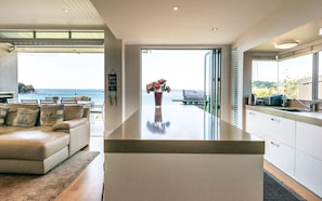 Uma cozinha moderna com vista para o mar, uma área de refeições com sofá e almofadas, e uma pequena ilha com um vaso de flores.