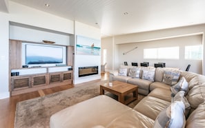 Uma sala de estar moderna com uma televisão de tela grande, lareira, sofá seccional e mesa de centro.