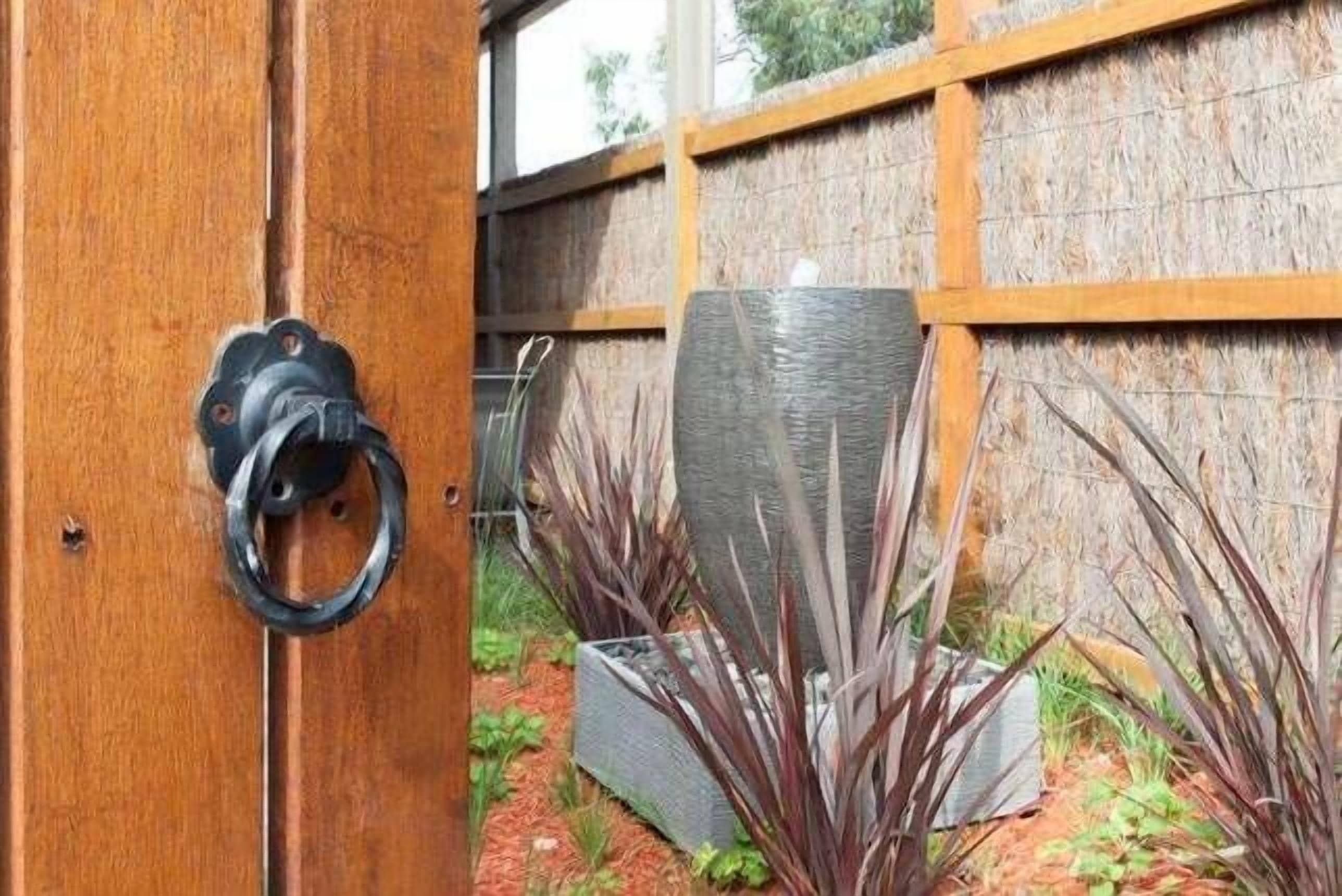 Eine Holztür mit Metallgriff, ein gewebter Korb und Pflanzen in einem Garten.