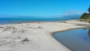 A beach with a clear sky, a small pool, and a distant mountain range. - Ruru Cottage - cosy native forest hideaway (Pakawau Beach)