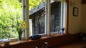 A kitchen with a window, a vase with flowers, and a sink. - Ruru Cottage - cosy native forest hideaway (Pakawau Beach)
