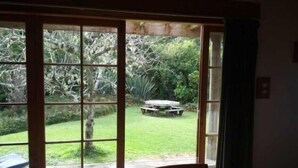 A room with a large sliding glass door leading to a garden with a picnic table. - Ruru Cottage - cosy native forest hideaway (Pakawau Beach)
