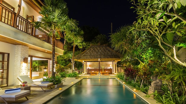 A swimming pool with lounge chairs, a thatched-roof structure, and lush greenery. - La Bali 4 Bedrooms Villa Sanur (Denpasar Selatan)