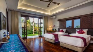A hotel room with two beds, a desk, a TV, and a large window with a view of greenery. - La Bali 4 Bedrooms Villa Sanur (Denpasar Selatan)