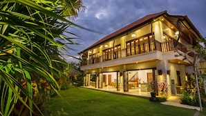 A two-story house with a balcony, surrounded by a well-maintained lawn and tropical plants. - La Bali 4 Bedrooms Villa Sanur (Denpasar Selatan)