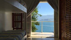 Quarto com cama, janela com cortinas e vista para o mar.