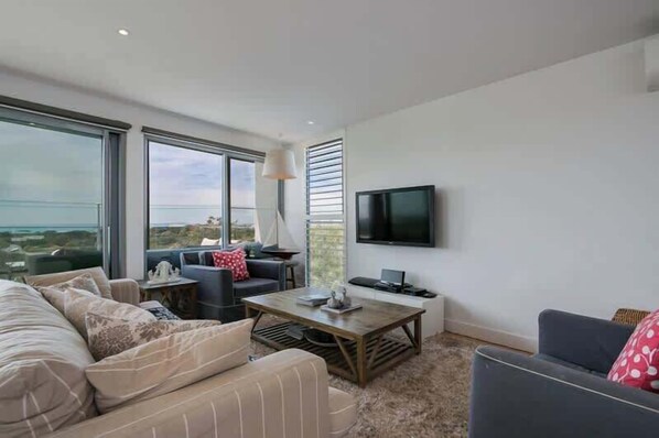 A modern living room with a sofa, armchairs, a coffee table, and a flat-screen TV mounted on the wall.