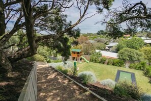 A backyard with a play area, a wooden deck, and a large tree. - Seaview Retreat (Blairgowrie)