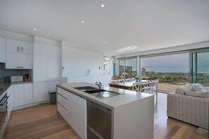A modern kitchen with a central island, a dining area with a view, and a large window. - Seaview Retreat (Blairgowrie)