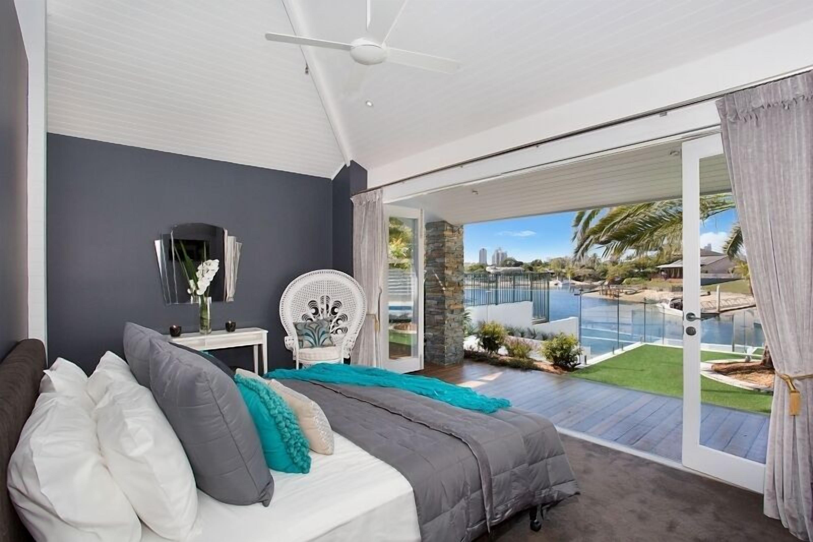 A bedroom with a bed, a chair, a nightstand, and a view of a swimming pool and garden.