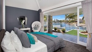 Une chambre à coucher comprenant un lit, une chaise, une table de chevet et donnant sur une piscine et un jardin.