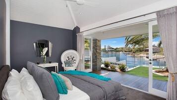 A bedroom with a bed, a chair, a nightstand, and a view of a swimming pool and garden.