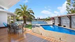 Un espace piscine extérieur moderne, doté d’une terrasse en bois, d’une table à manger avec des chaises et offrant une vue sur l’océan.