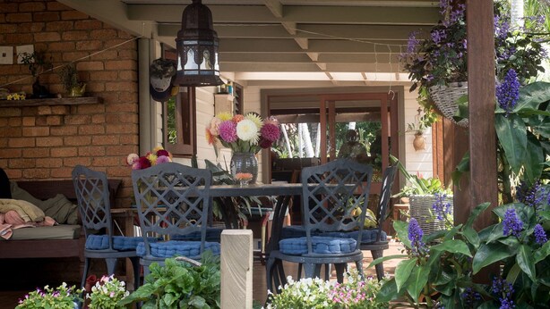 A covered outdoor seating area with a table and chairs, surrounded by potted plants and flowers. - The Rosebank Farmhouse (Rosebank)