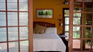 A bedroom with a bed, a wooden headboard, a nightstand, and a window with a view of greenery. - The Rosebank Farmhouse (Rosebank)