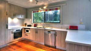 A modern kitchen with wooden cabinets, stainless steel appliances, a window with a view of greenery, and a red toaster.