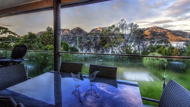 A table with chairs and a decorative bird sculpture, overlooking a lake with mountains in the background.