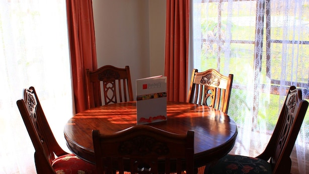 A round wooden dining table with a white box labeled "Hatcher's Manor" in the center, surrounded by four wooden chairs with intricate back designs. - Hatcher's Manor Richmond - Farmhouse (Richmond TAS)