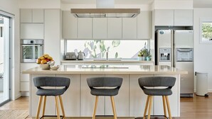 Eine moderne Küche mit einer zentralen Kochinsel, drei Barhocker, einem Einbauofen und einem Kühlschrank.