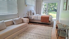 A bedroom with a bed, a sofa, a small table, and a view of the outdoors. - Werri Escape - walk to the beach (Gerringong)