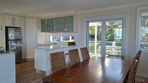 A modern kitchen with white cabinets, a stainless steel refrigerator, and a large island with bar stools. - Werri Escape - walk to the beach (Gerringong)