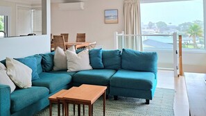 A modern living room with a teal sectional sofa, a wooden coffee table, and a view of the beach through large windows. - Werri Escape - walk to the beach (Gerringong)