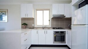 A modern kitchen with white cabinets, a stainless steel oven, and a window above the sink.
