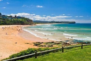 A beach with a wooden fence, people swimming, and buildings in the background.