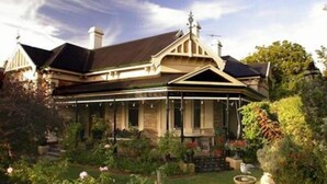 A Victorian-style house with a prominent gabled roof, a conservatory, and a well-maintained garden with various plants and a birdbath. - Bishops Garden Spa Suite (North Adelaide)