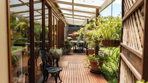 A covered patio with wooden flooring, a table and chairs, and potted plants. - Bishops Garden Spa Suite (North Adelaide)