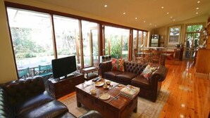 A spacious living room with a large wooden coffee table, leather sofas, and a television. - Bishops Garden Spa Suite (North Adelaide)