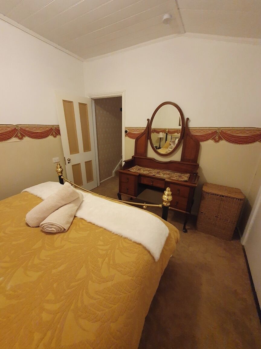 A hotel room with a bed, a dresser with a mirror, and a door leading to another room.