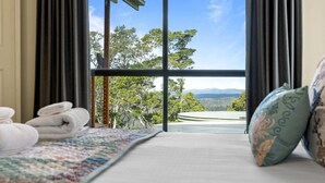Une chambre d’hôtel avec une grande fenêtre, un lit recouvert d’une courtepointe aux couleurs vives, et une vue sur les arbres et les montagnes.