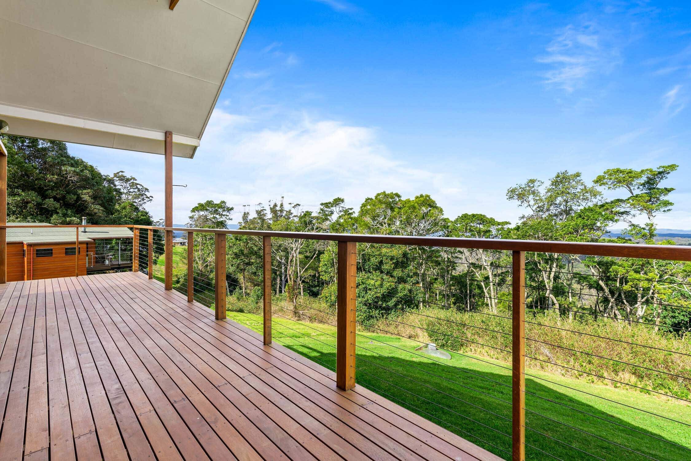 A wooden deck with a metal railing overlooking a well-maintained lawn and trees.