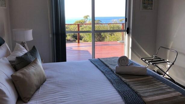 Et hotelv ærelse med en stor seng, havudsigt gennem en skydedør, en balkon og et metalstativ til tøj.