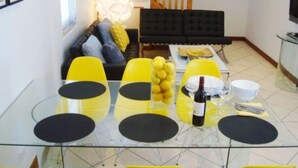 Un coin repas avec une table en verre, des chaises jaunes et un canapé noir en arrière-plan.