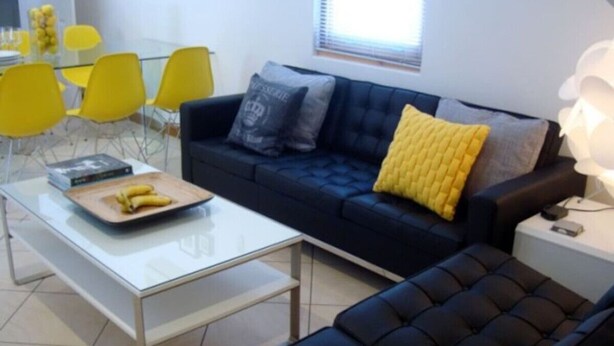 Un salon moderne avec un canapé bleu foncé, une table basse blanche et des chaises jaunes.