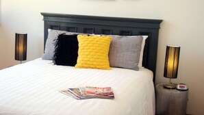 Un lit bien fait, avec une couette blanche, deux oreillers et un magazine posé sur le lit. Deux lampes de chevet sont placées de chaque côté du lit.