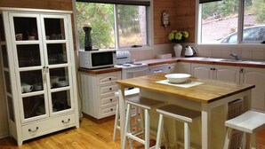 A kitchen with white cabinets, a wooden countertop, a microwave, a stove, and a sink.