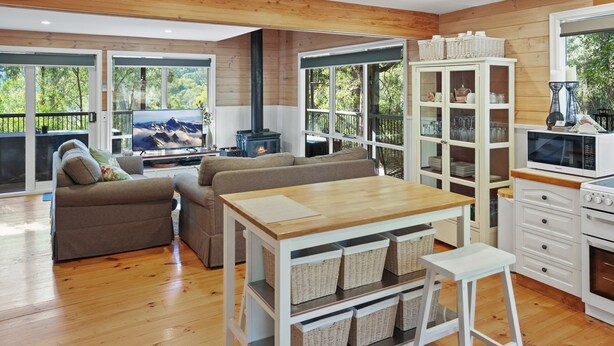 A modern living room with a sofa, TV, fireplace, dining table, and kitchen area with cabinets and appliances.