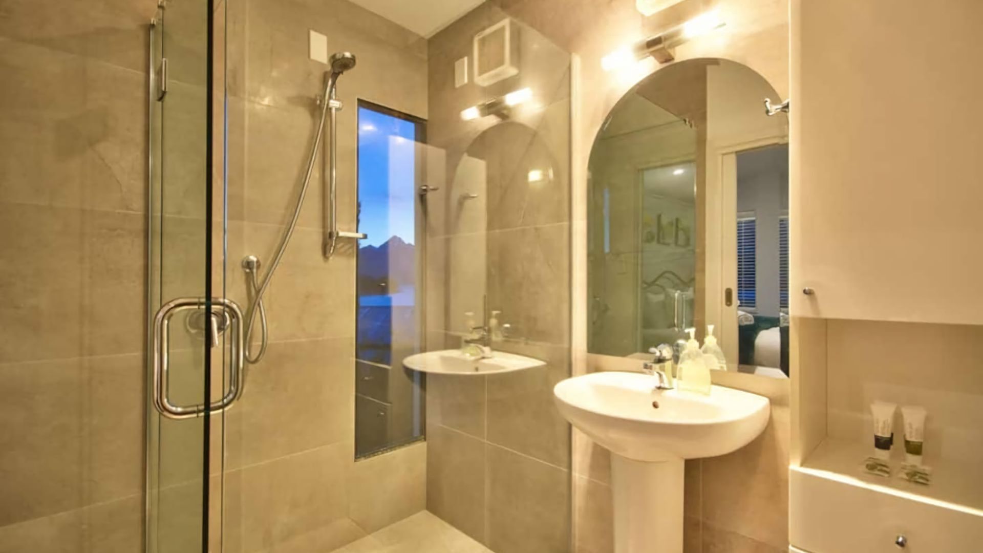 Une salle de bain moderne avec une douche à parois de verre, deux lavabos et un grand miroir.
