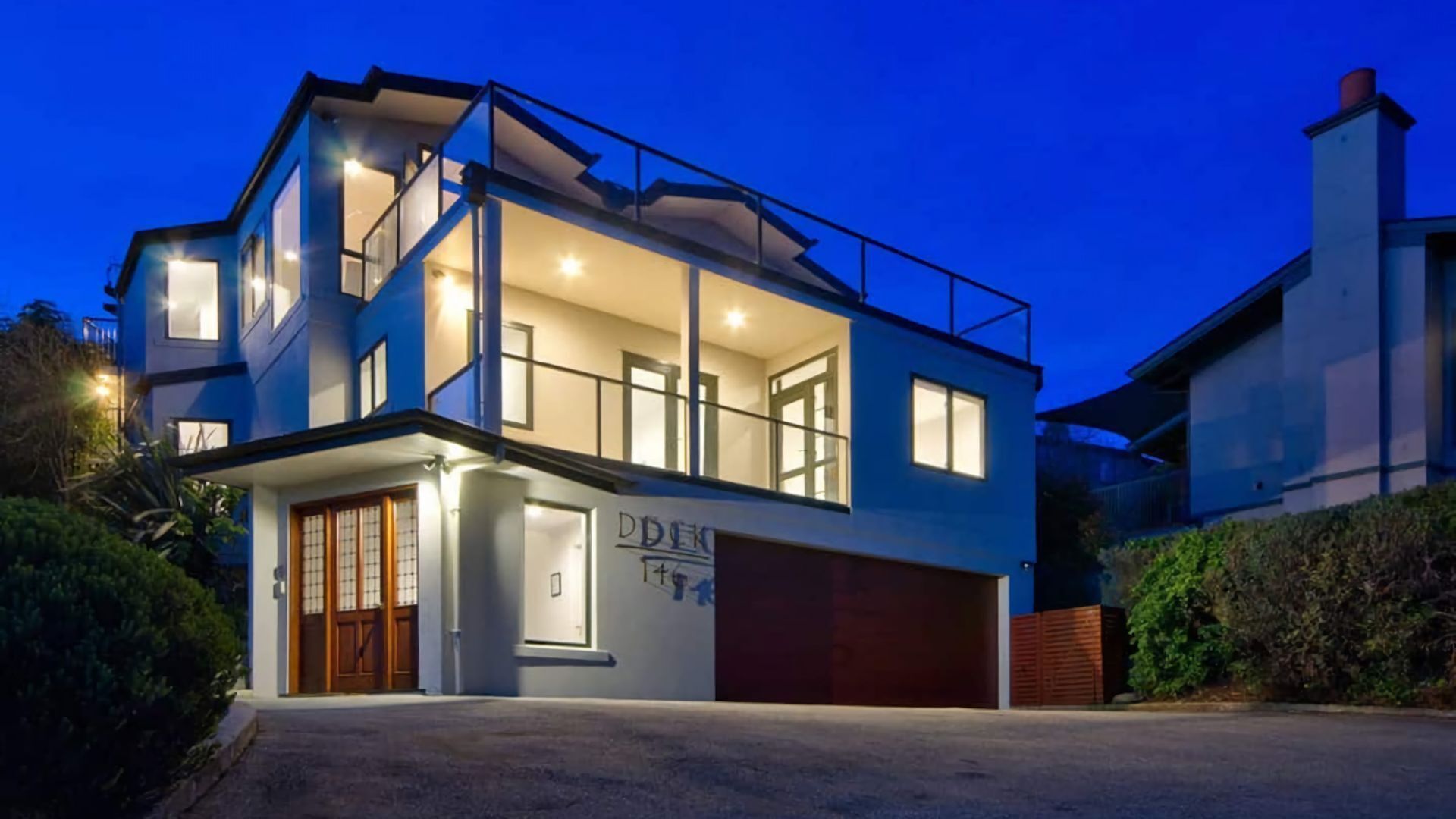 A modern two-story house with a garage, large windows, and a balcony.