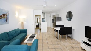Un salon moderne avec un canapé de couleur turquoise, une table basse, un téléviseur et un coin repas comprenant des chaises et une table.