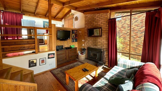 A cozy cabin interior with a wooden ceiling, a fireplace, a television, and a sofa.